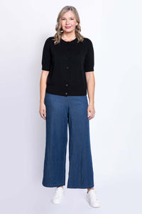 Woman facing forward in a black button-up short-sleeve cardigan, blue wide-leg pants, and white shoes