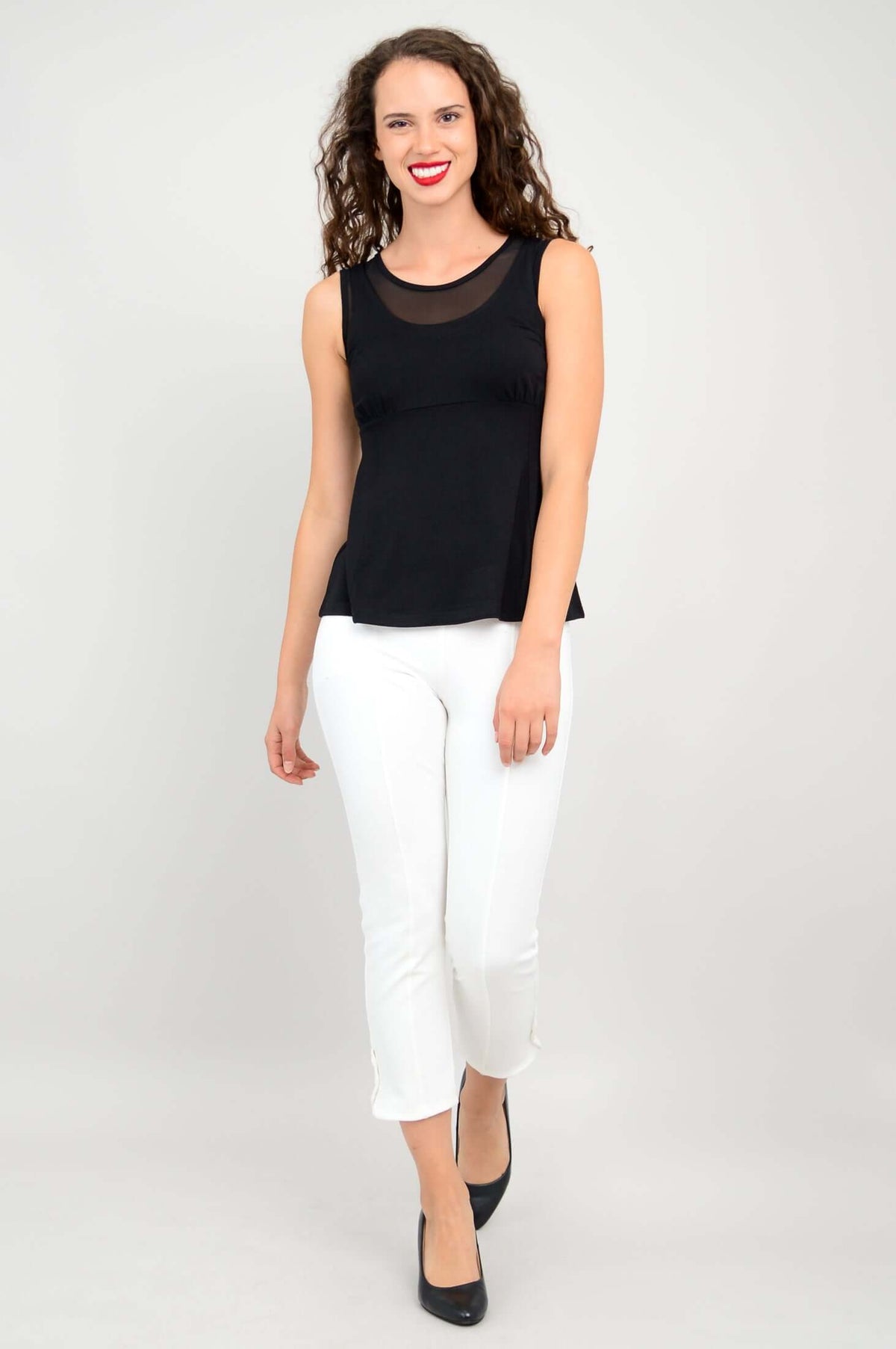 Woman facing side in black mesh tank top paired with white cropped pants