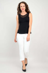 Woman facing side in black mesh tank top paired with white cropped pants