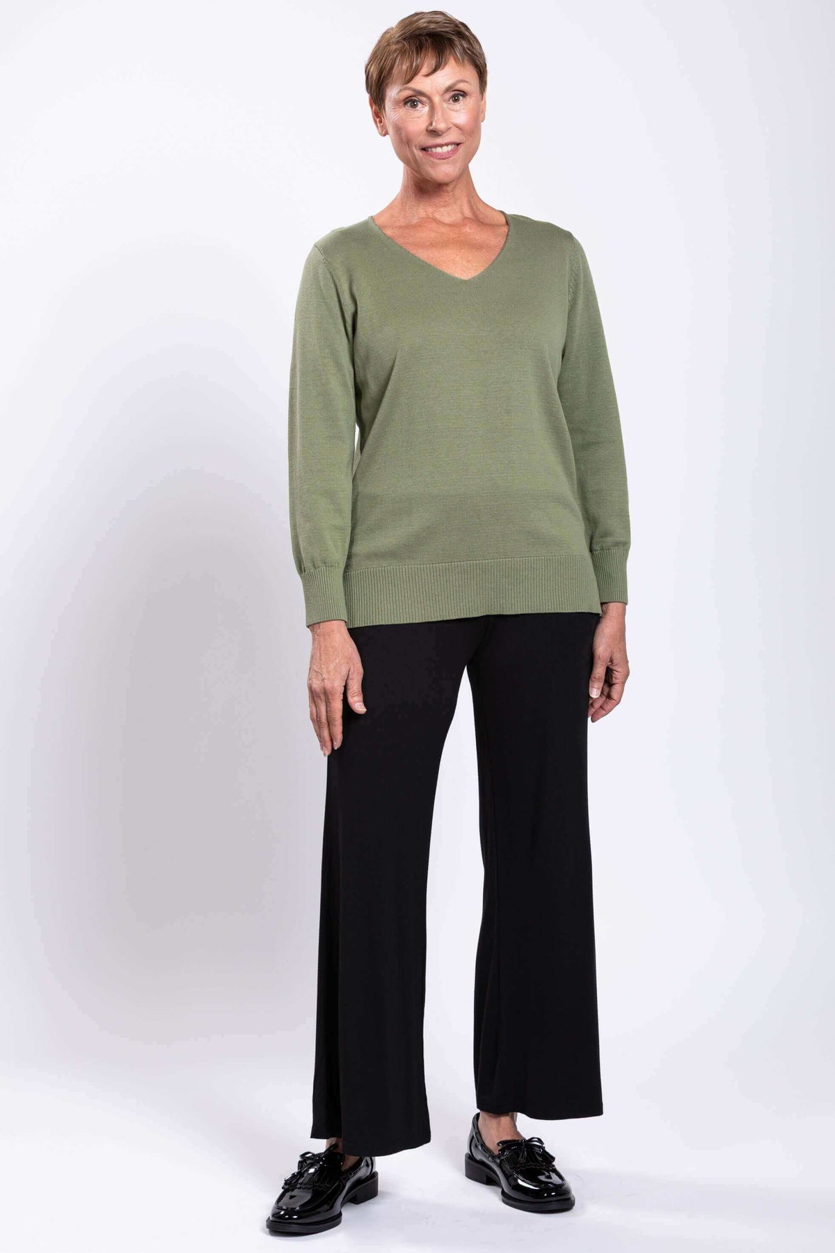 Front-facing woman in green V-neck cotton sweater and black pants