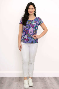 Woman standing, front view, in purple mandala print bamboo top and white pants