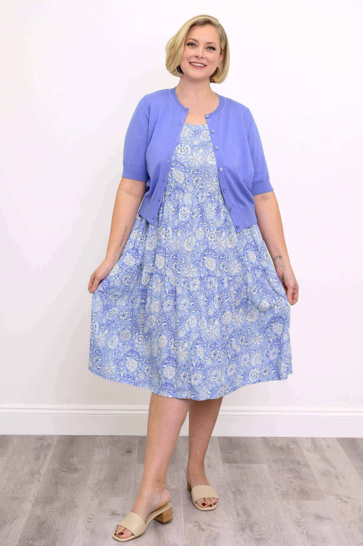 Woman in a blue floral tiered dress and light purple cardigan, holding the skirt