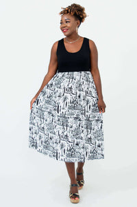 Woman posing in a sleeveless city print midi dress, holding out the skirt for display