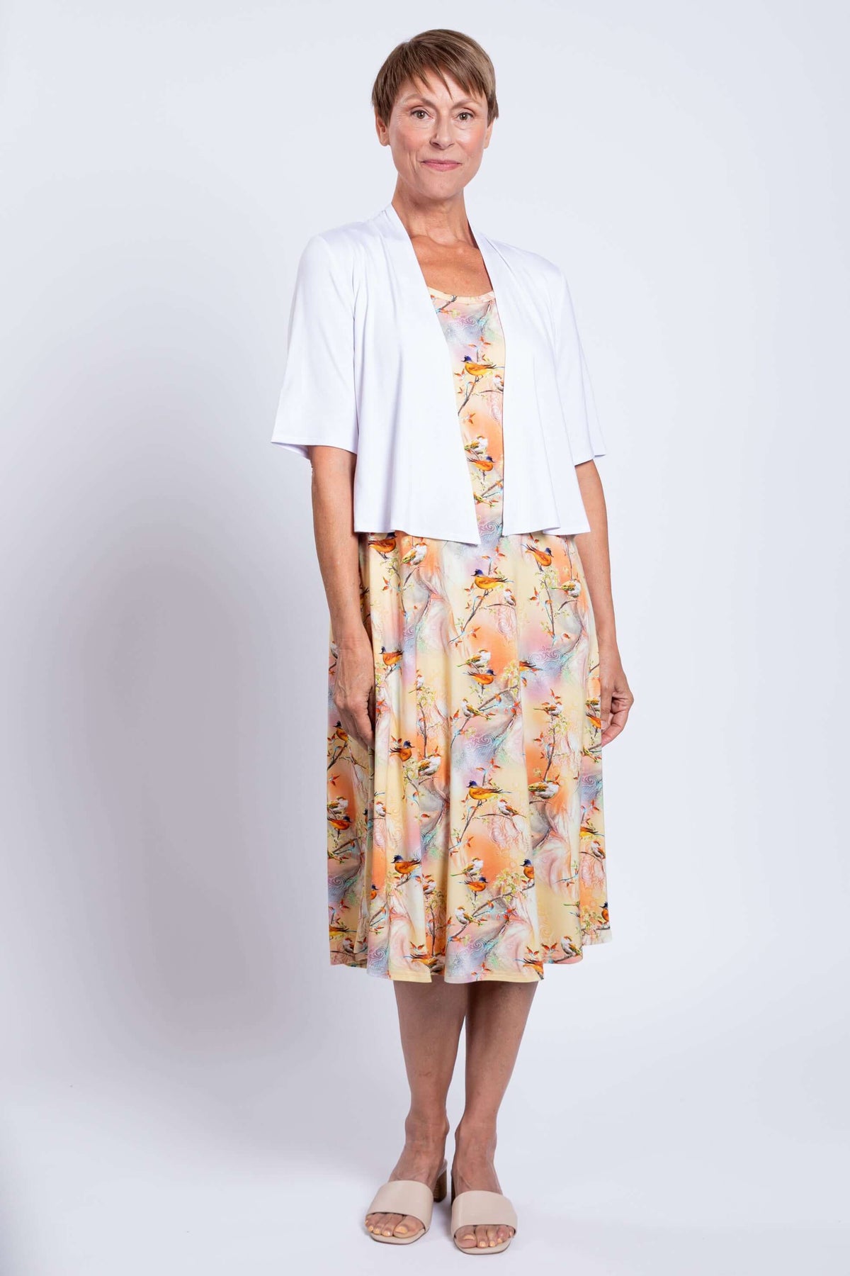 Woman in Birds of Paradise print dress and white shrug, standing front-facing