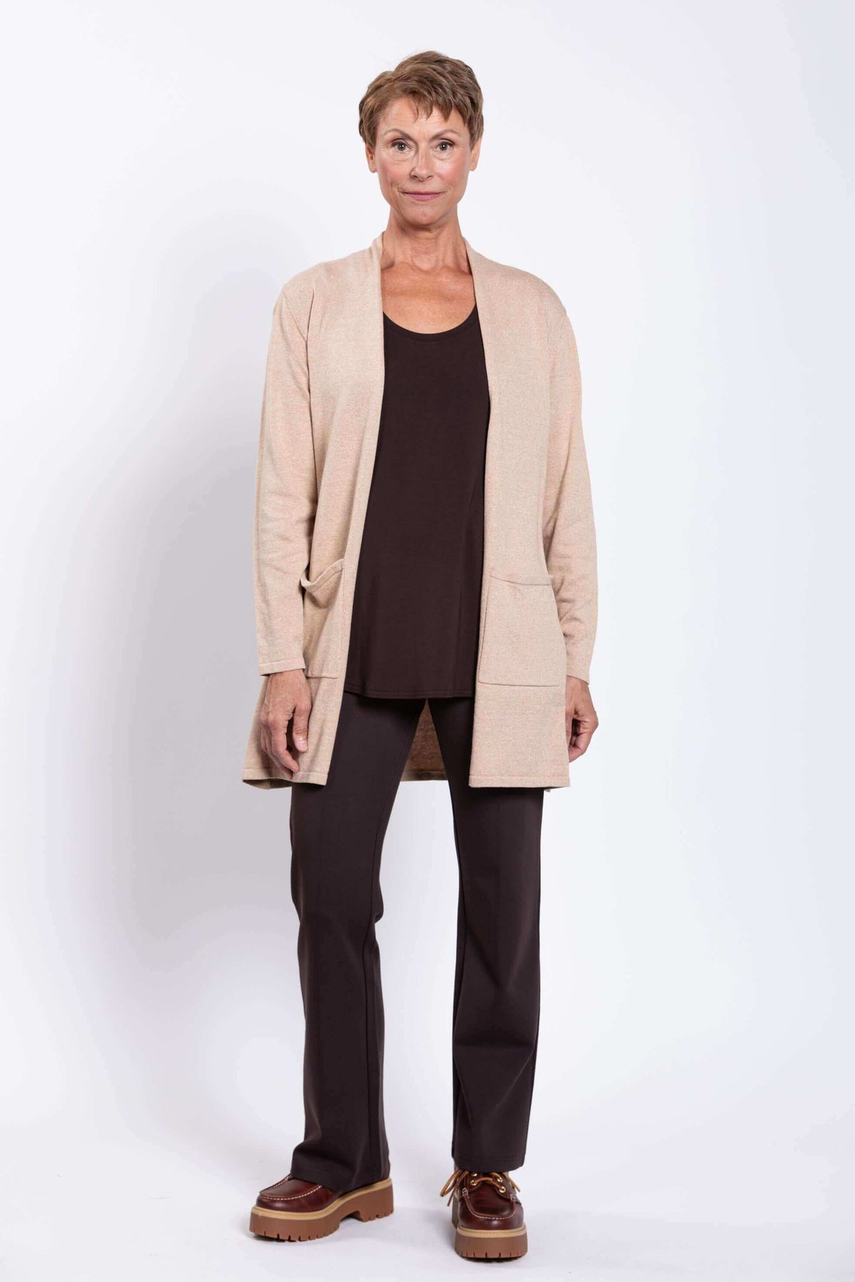 Woman standing in neutral cardigan with open front and large pockets, brown pants and shoes