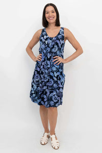 Woman standing with hands on hips, wearing a navy blue sleeveless floral dress with pockets