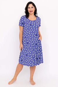 Woman wearing a purple polka dot short-sleeve sleepshirt, standing and smiling