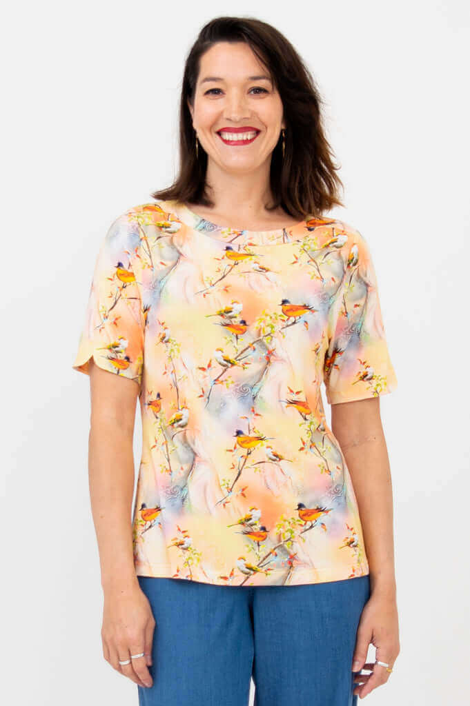 Woman wearing a peach-colored short sleeve top with a colorful birds print, smiling