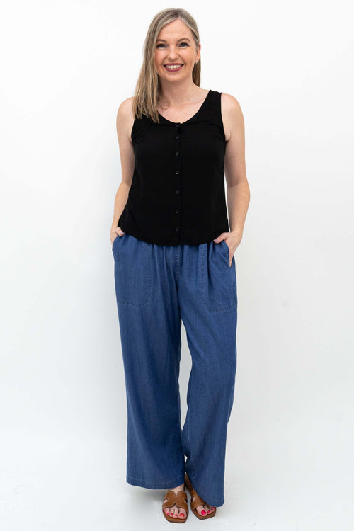 Woman wearing black sleeveless top and wide-leg blue denim Tencel pants with hands in pockets