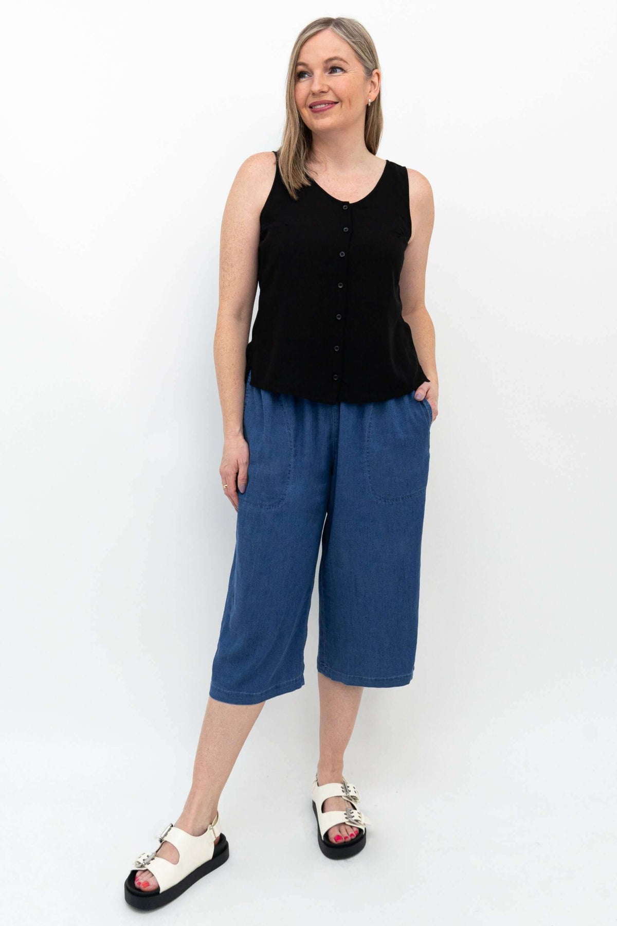 Woman in blue denim Tencel capris and black sleeveless top smiling