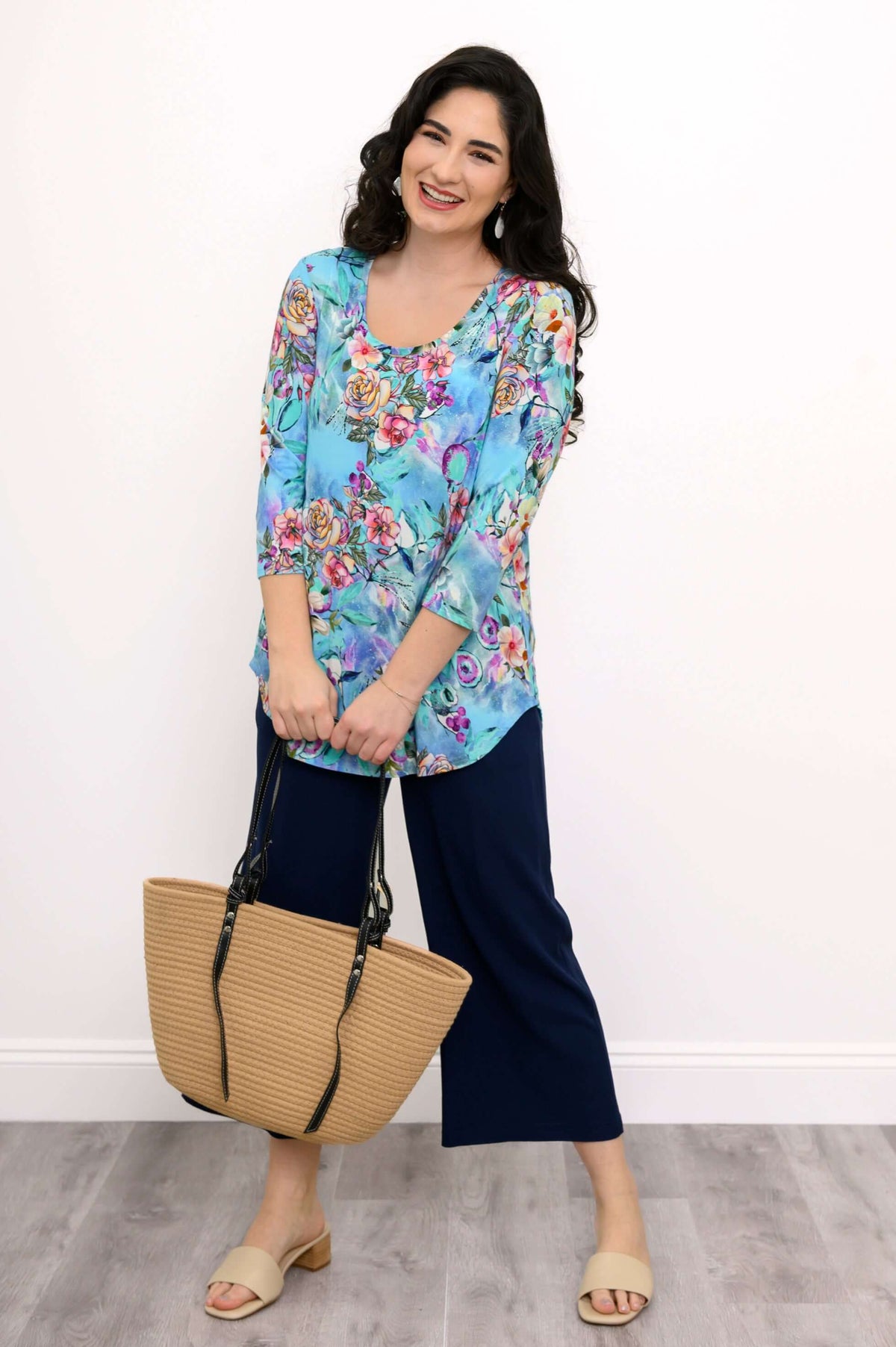 Woman in a blue floral bamboo top holding a tan tote bag, full body view