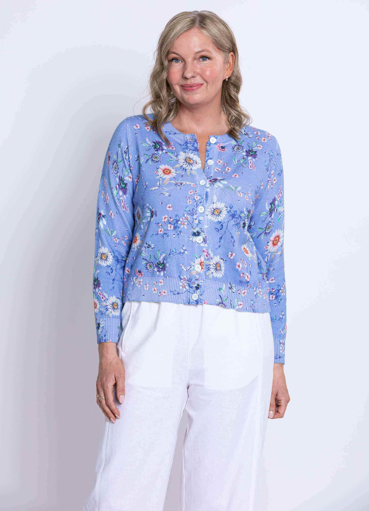 Woman in a blue floral cardigan and white wide-leg pants, angled forward