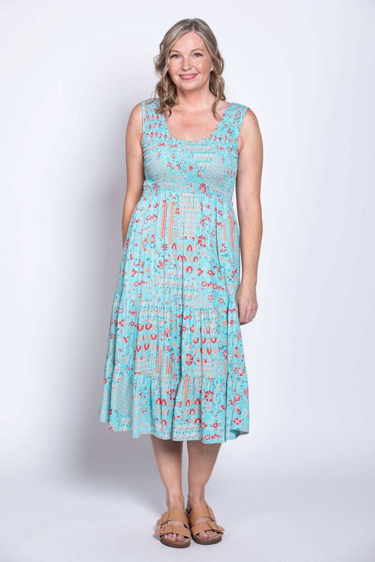 Woman in a blue floral sleeveless dress, standing and smiling at the camera