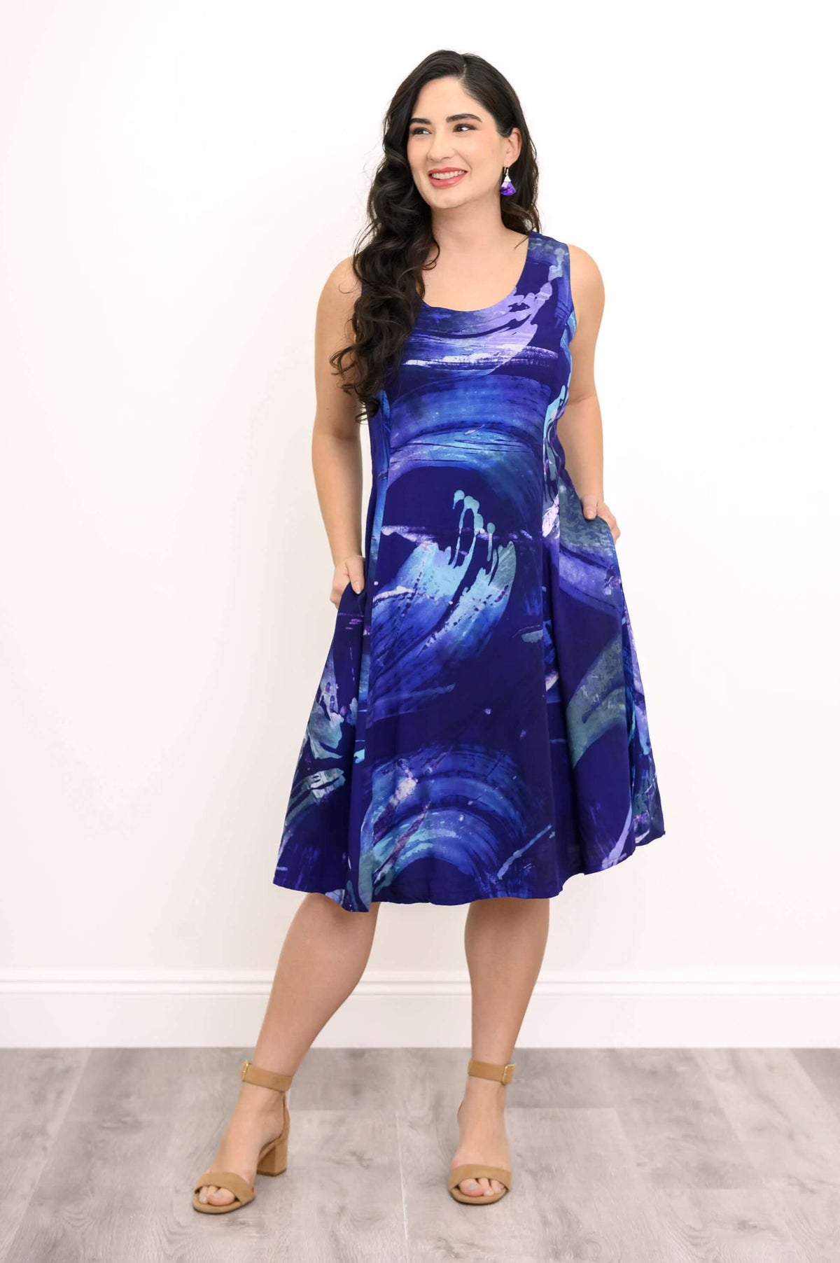 Woman in a blue swirl sleeveless dress with hands in pockets, posing confidently