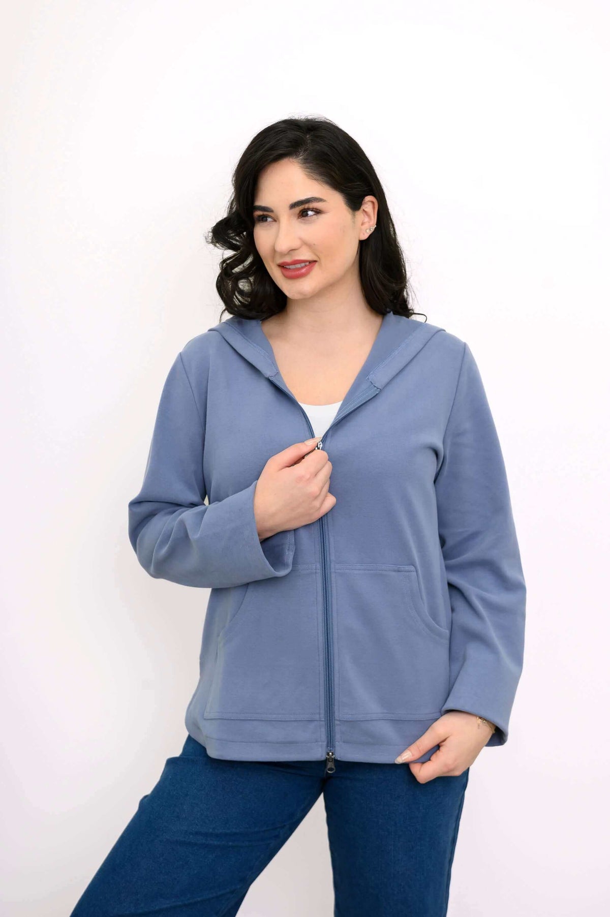 Woman in a blue zip-up hoodie, holding the zipper, looking to the side