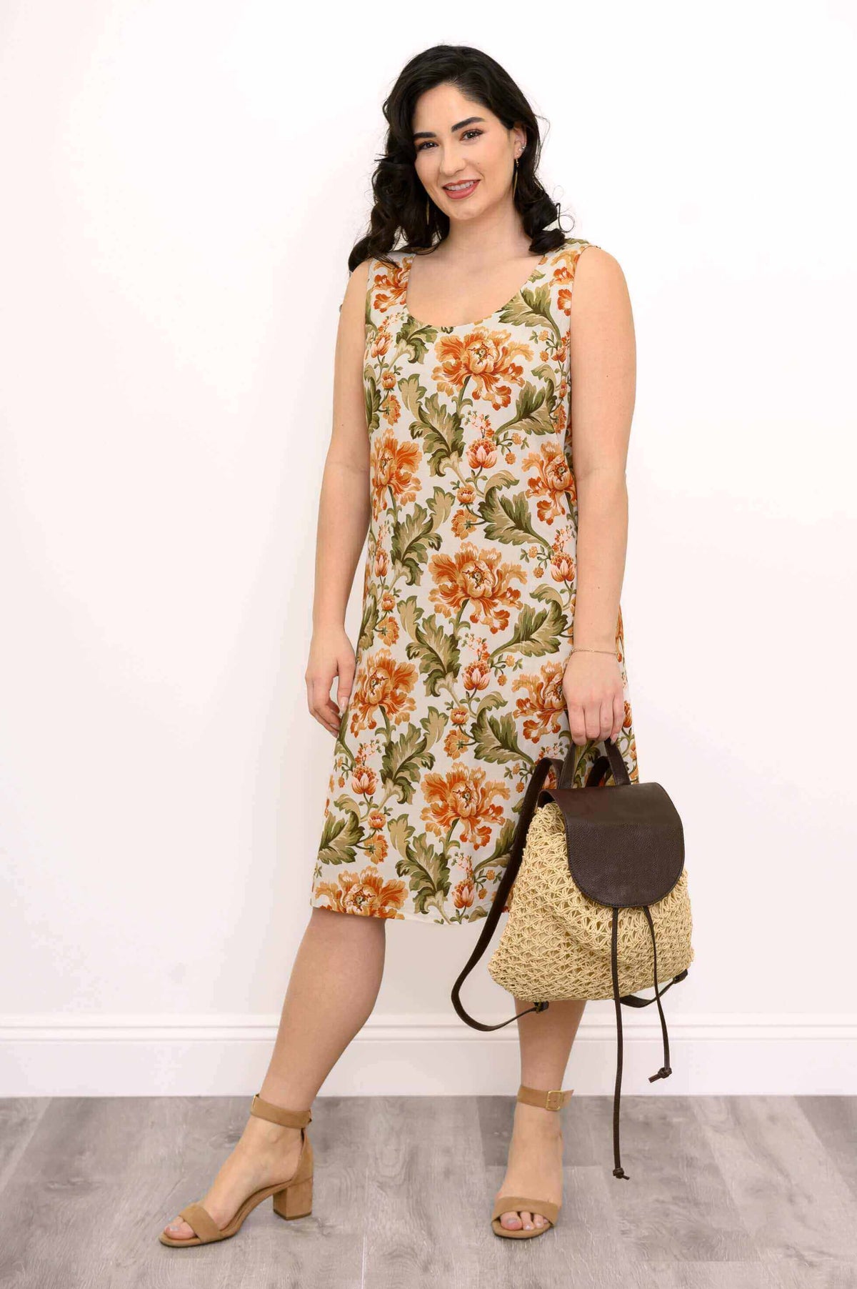 Woman in a floral sleeveless dress holding a woven straw backpack