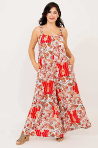 Woman in a flowing red and cream floral jumpsuit posing with hands in pockets