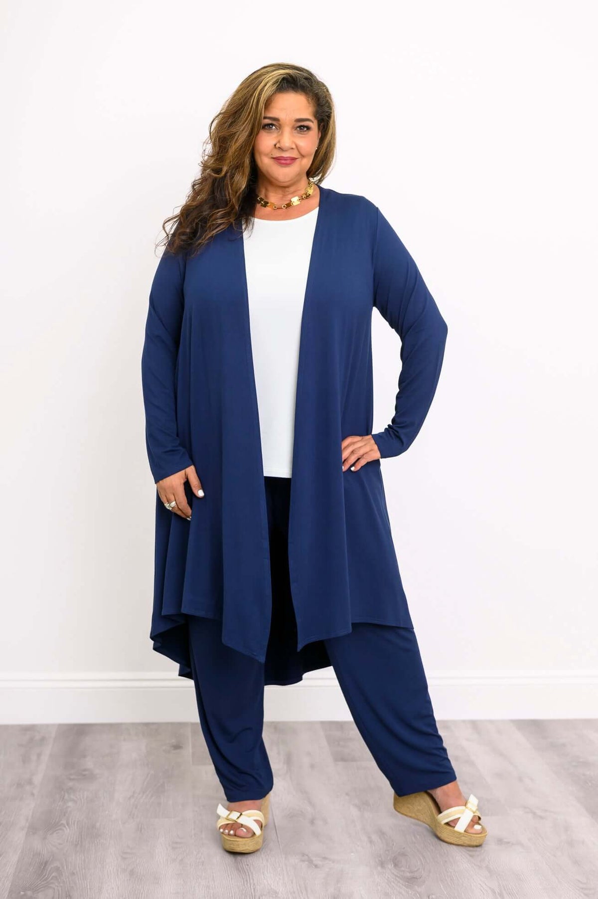 Woman in a navy blue high-low duster cardigan and pants, with white heeled sandals