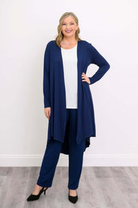 Woman in a navy blue high-low duster cardigan, white top, and navy pants, hand on hip