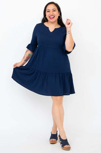 Woman in a navy empire waist dress holding out the skirt and smiling widely