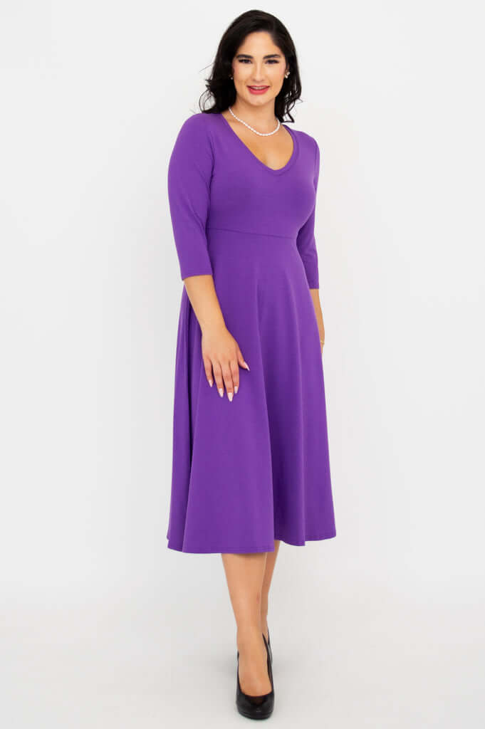 Woman in a purple midi dress posing with hand on hip, displaying the empire waist
