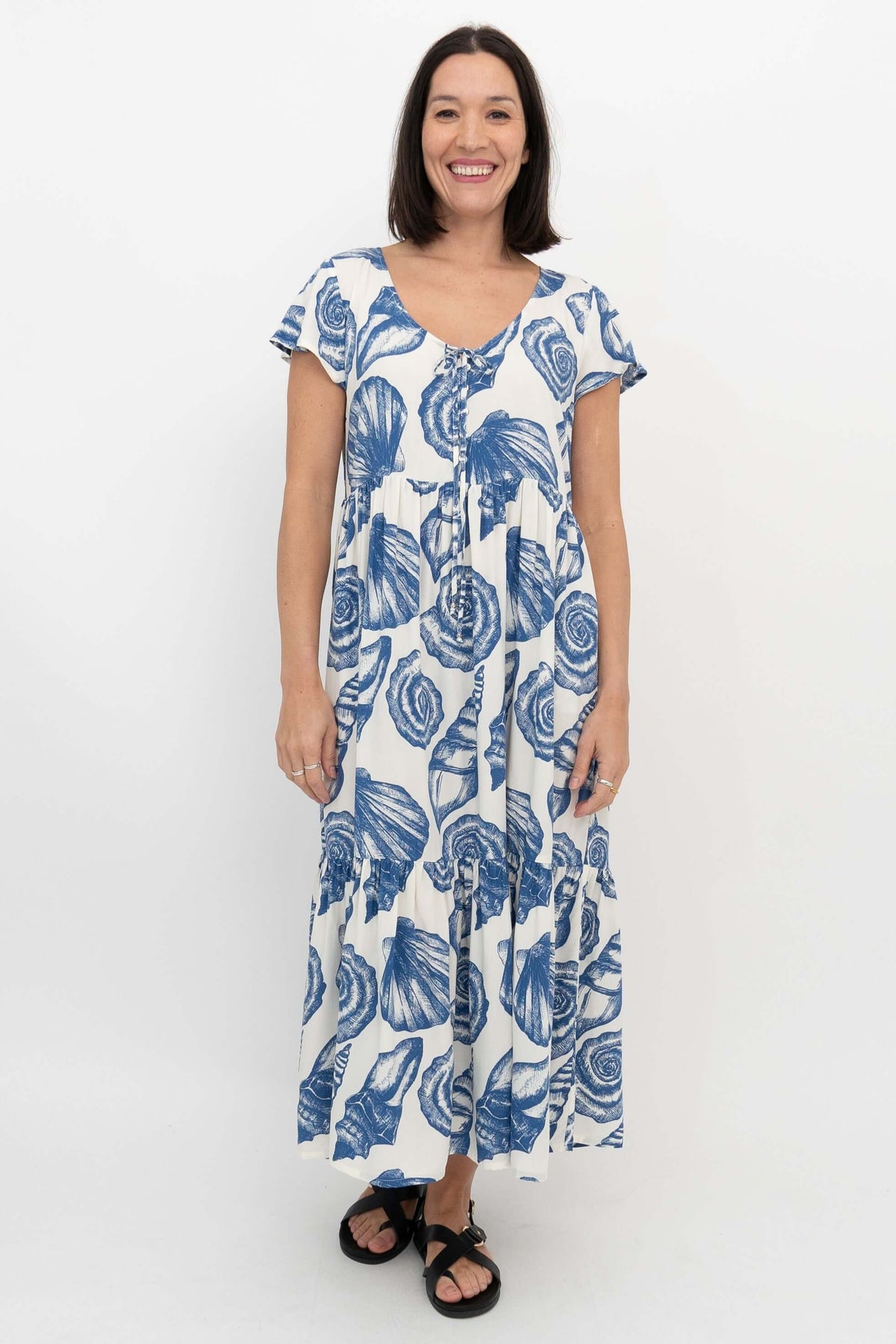 Woman in a white dress with blue seashell pattern, standing straight facing forward