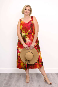 Woman in a colorful sleeveless midi dress holding a straw hat in front, standing on a wood floor