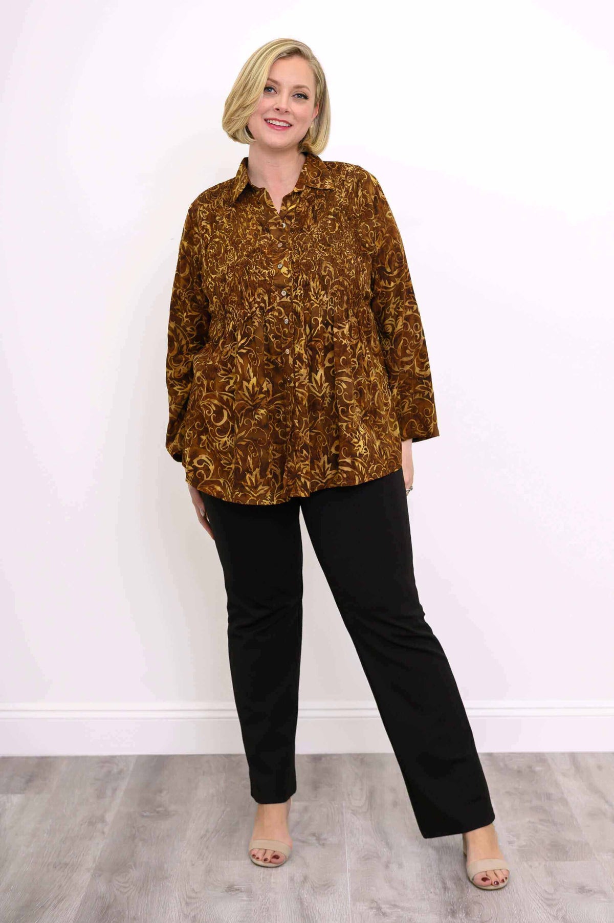 Woman in autumn gold smocked shirt standing with relaxed pose, black trousers and heels