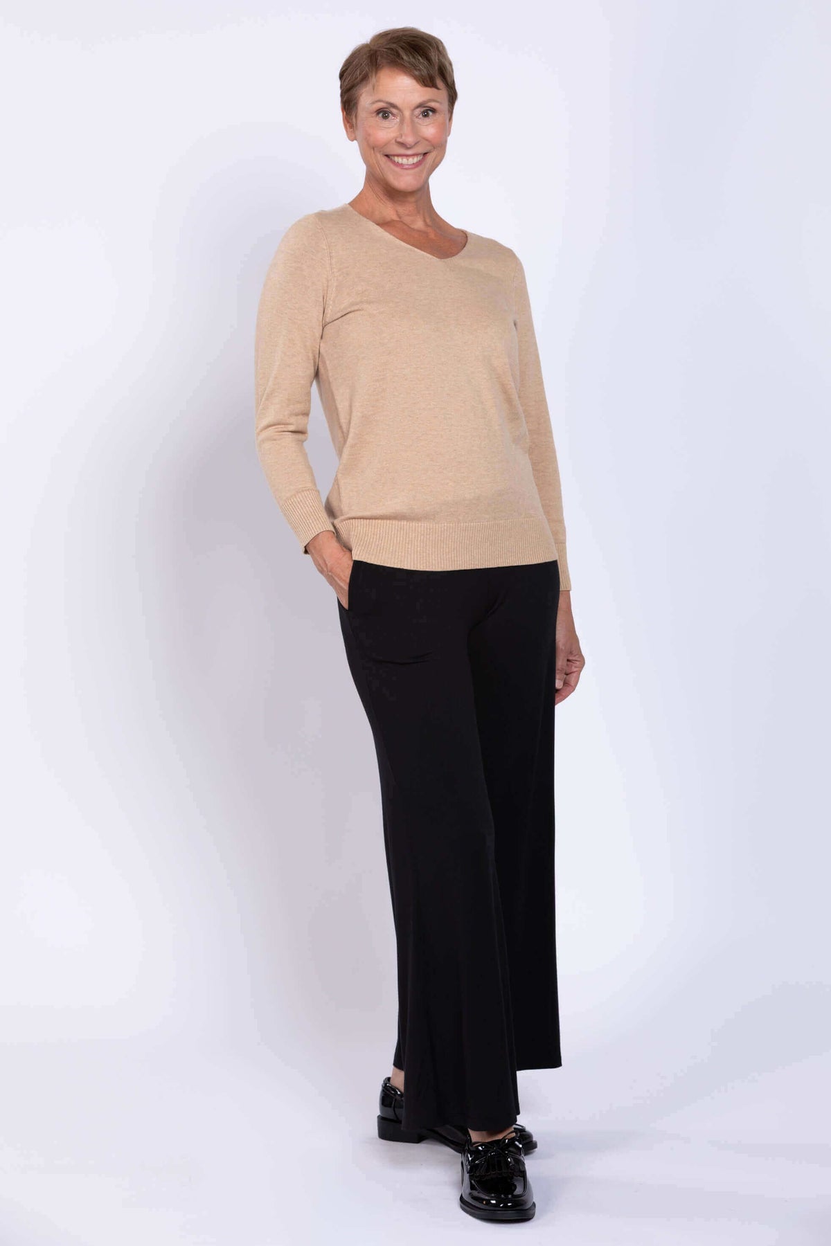 Woman in beige V-neck cotton sweater and black slacks, hands in pockets