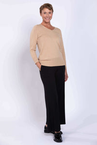 Woman in beige V-neck cotton sweater and black slacks, hands in pockets