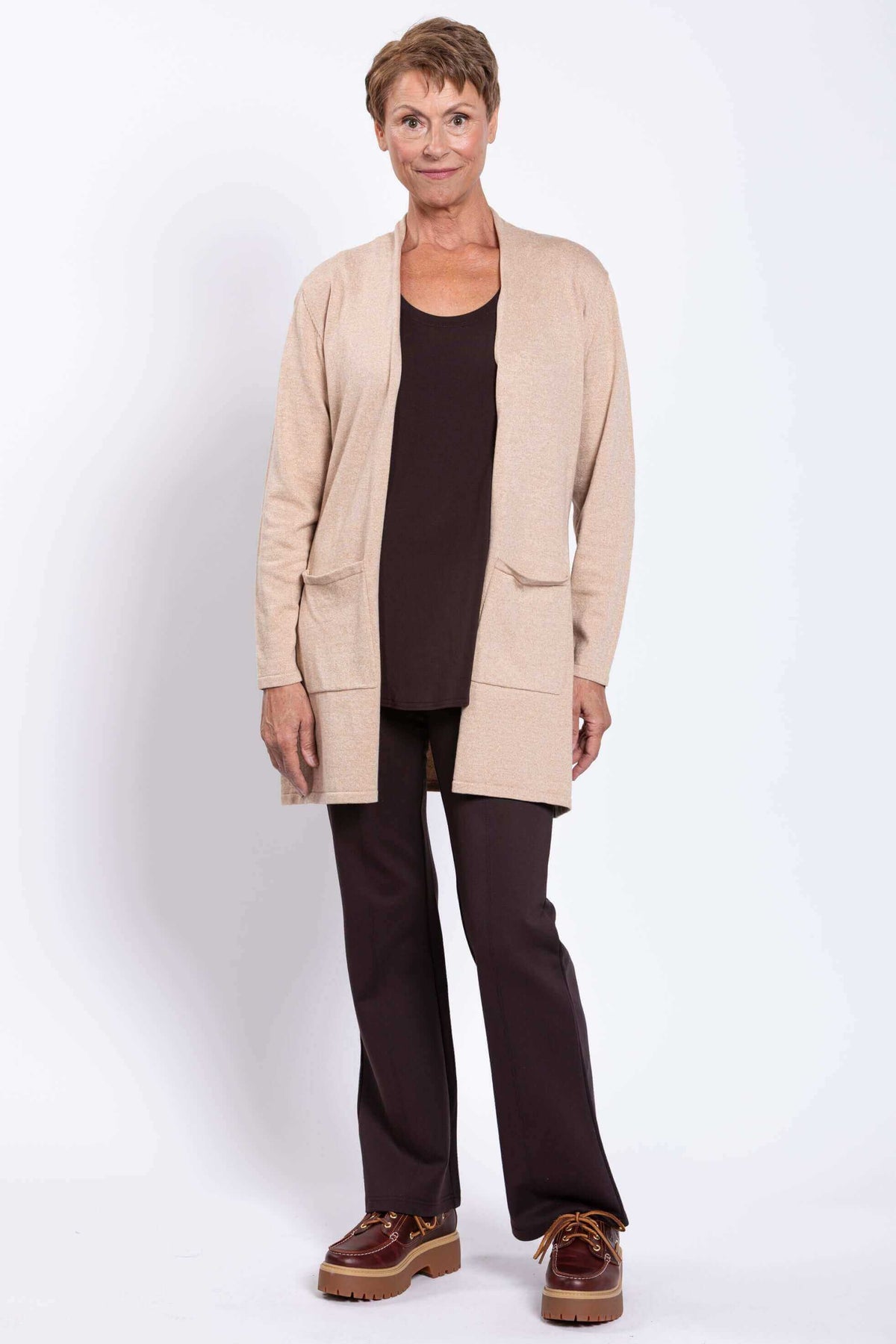 Woman standing in a beige cardigan, dark brown top and pants, facing forward