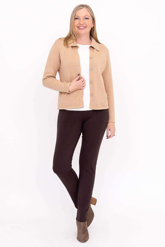 Woman in beige collared cardigan, brown pants, and taupe boots standing with hand in pocket
