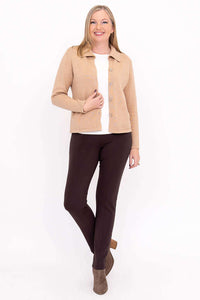 Woman in beige collared cardigan, brown pants, and taupe boots standing with hand in pocket