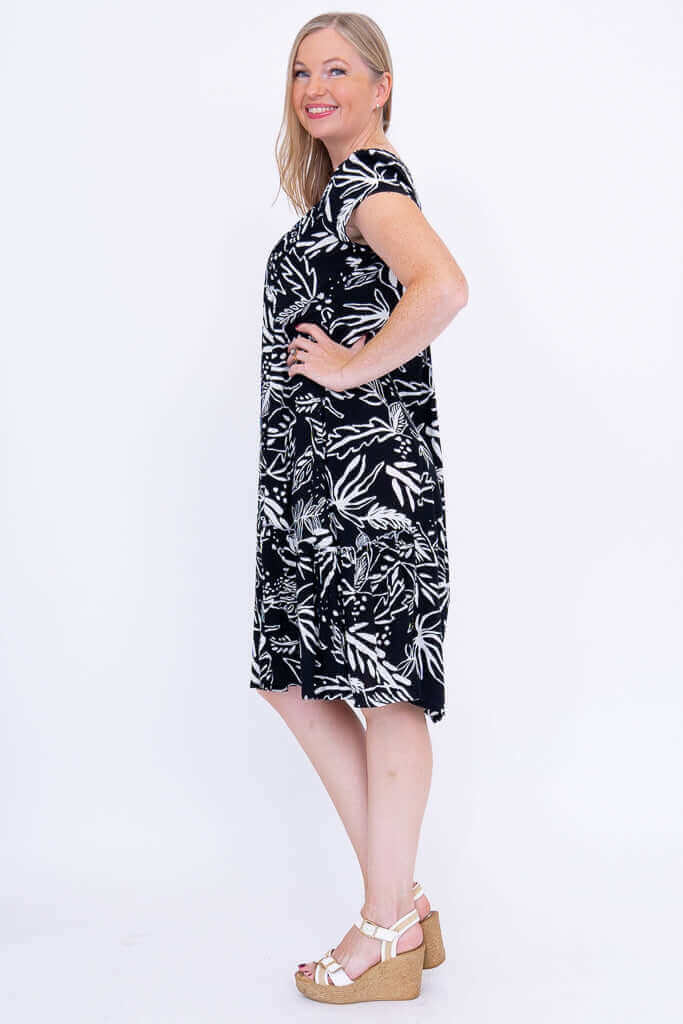 Woman in black and white leaf print dress, side profile with hand on hip
