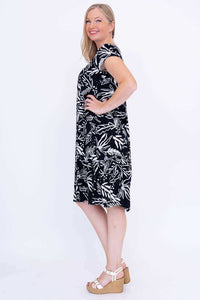 Woman in black and white leaf print dress, side profile with hand on hip