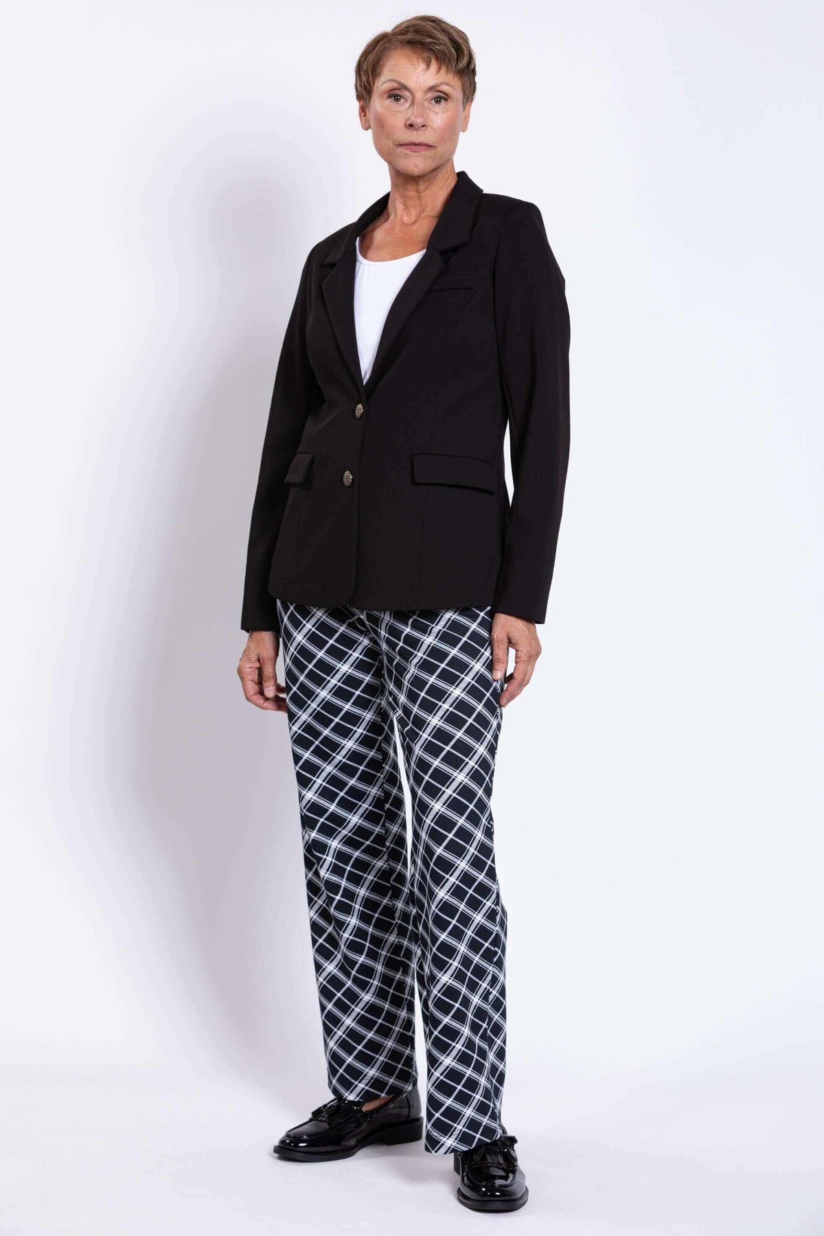 Woman standing in black blazer and checked pants, front angle view