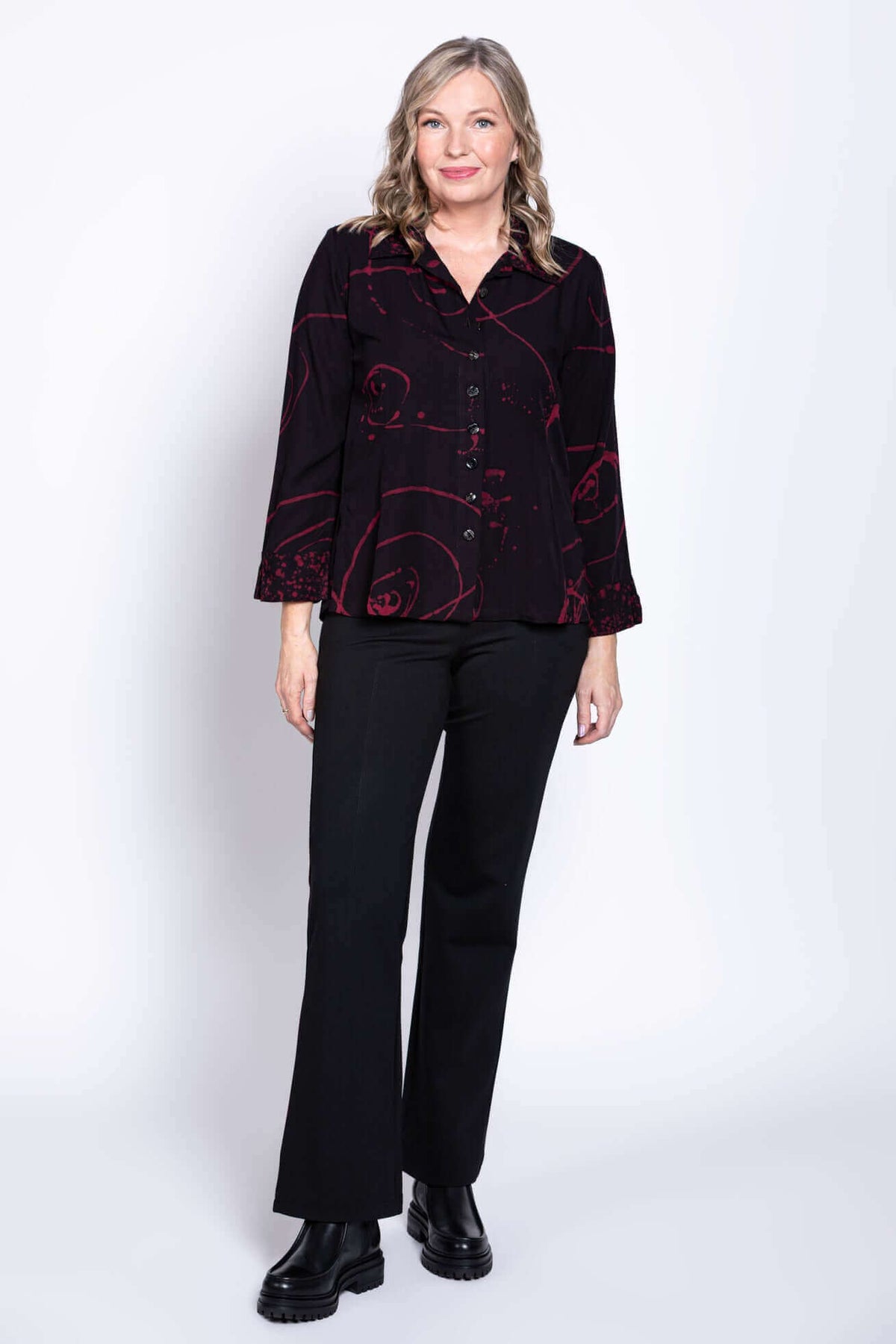 Standing woman in black blouse with maroon abstract patterns and black trousers