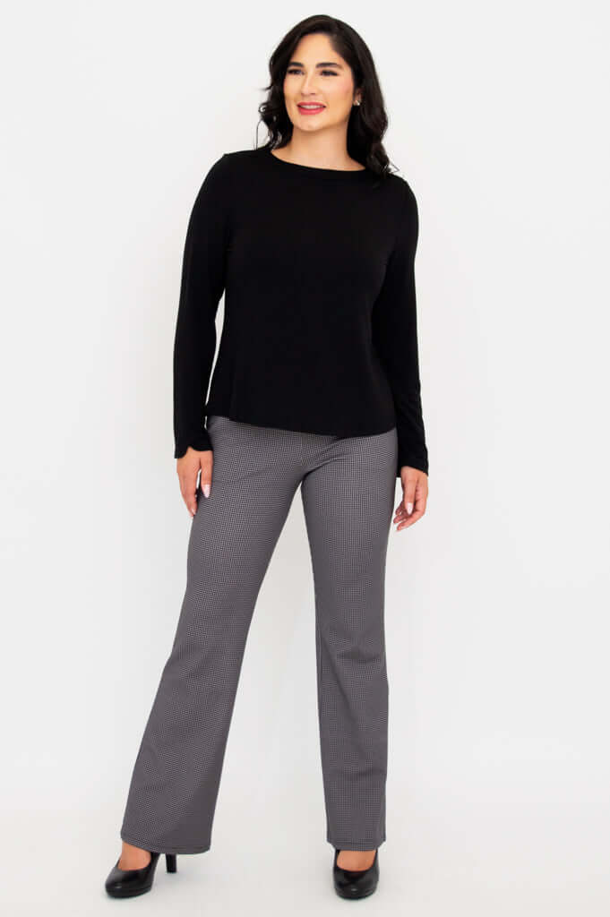 Smiling woman in black boat neck top and gray check pants, hands at sides