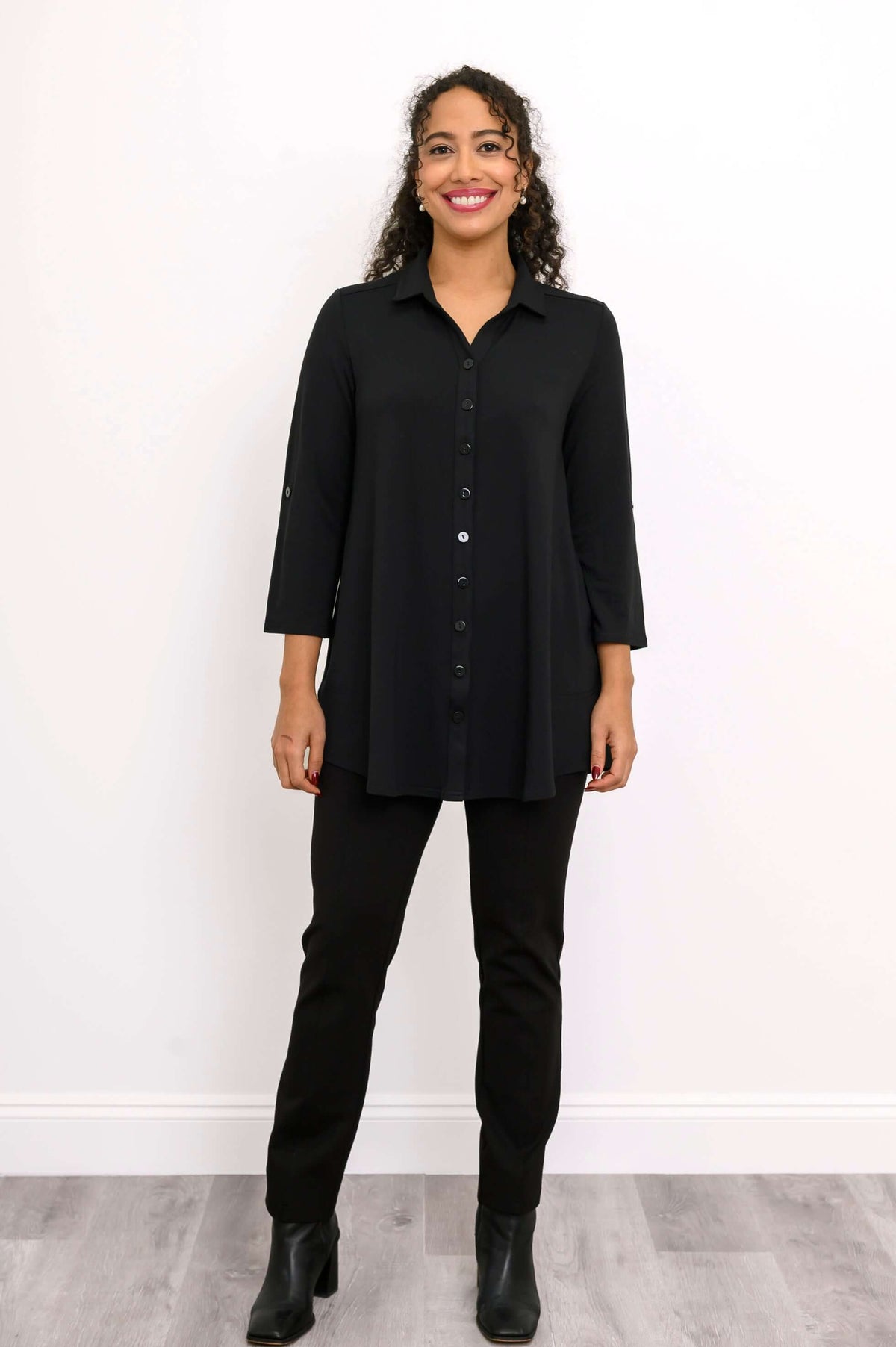 Woman in black buttoned blouse-jacket and pants, standing straight