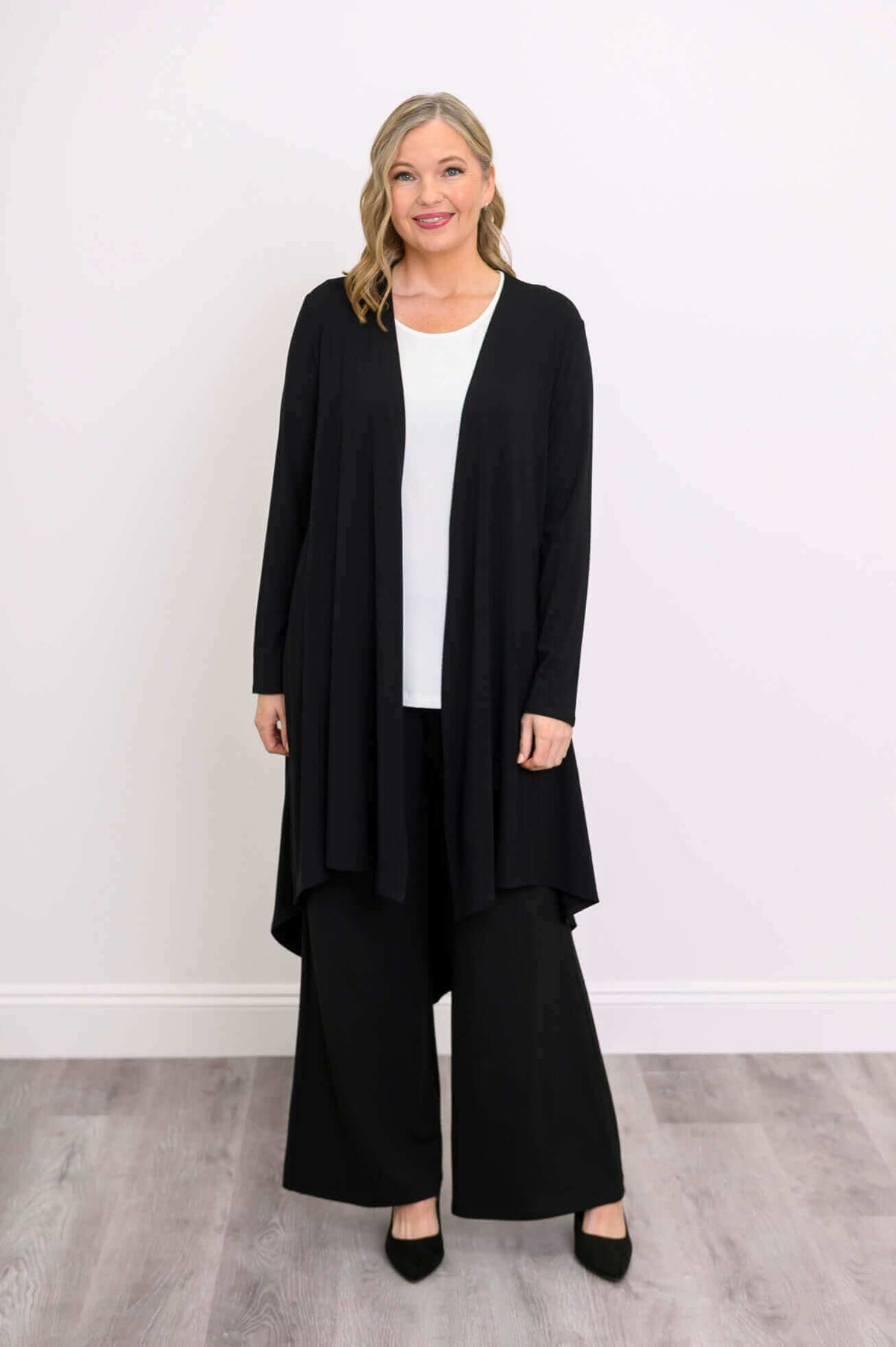 Woman in black high-low hem duster cardigan over white top, facing forward