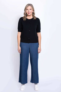 Front-centered full length of a woman in a black short-sleeve cardigan and wide-leg pants