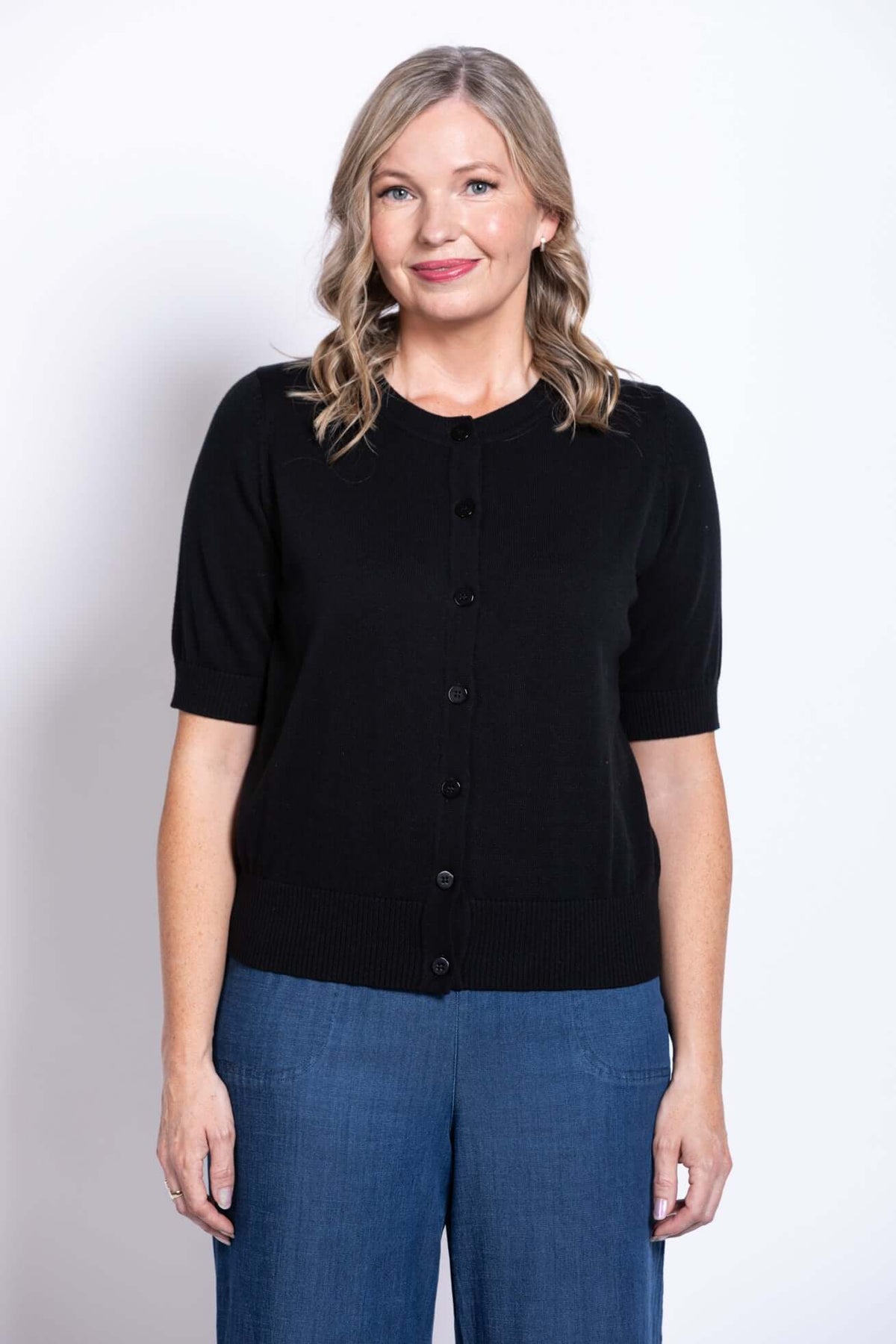 Woman wearing a black short-sleeve button-up cardigan with blue wide-leg pants, front view