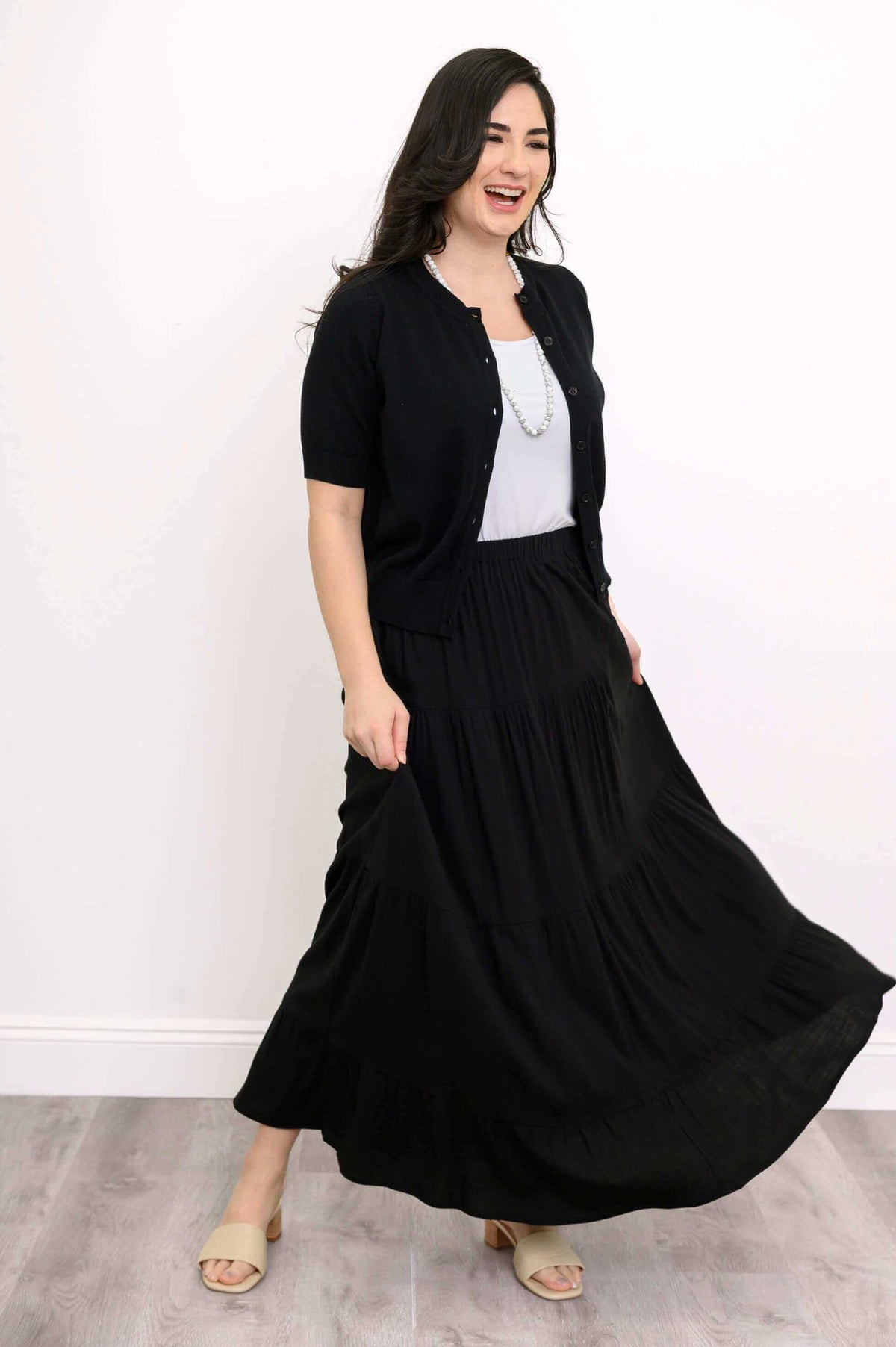 Woman in a black tiered maxi skirt, white top, and black cardigan, smiling