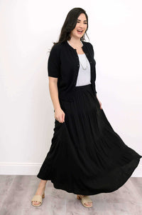 Woman in a black tiered maxi skirt, white top, and black cardigan, smiling
