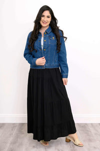Woman wearing a black tiered maxi skirt paired with a denim jacket and sandals