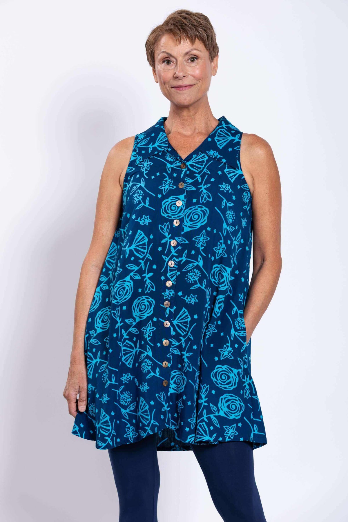 Woman wearing a sleeveless blue A-line tank with floral print, button-up front, and pockets