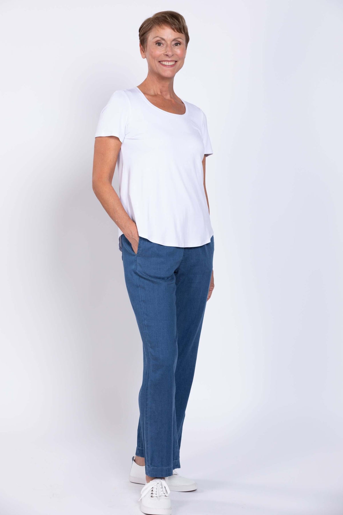 Full body front view of woman wearing white short sleeve shirt with lightweight denim pants
