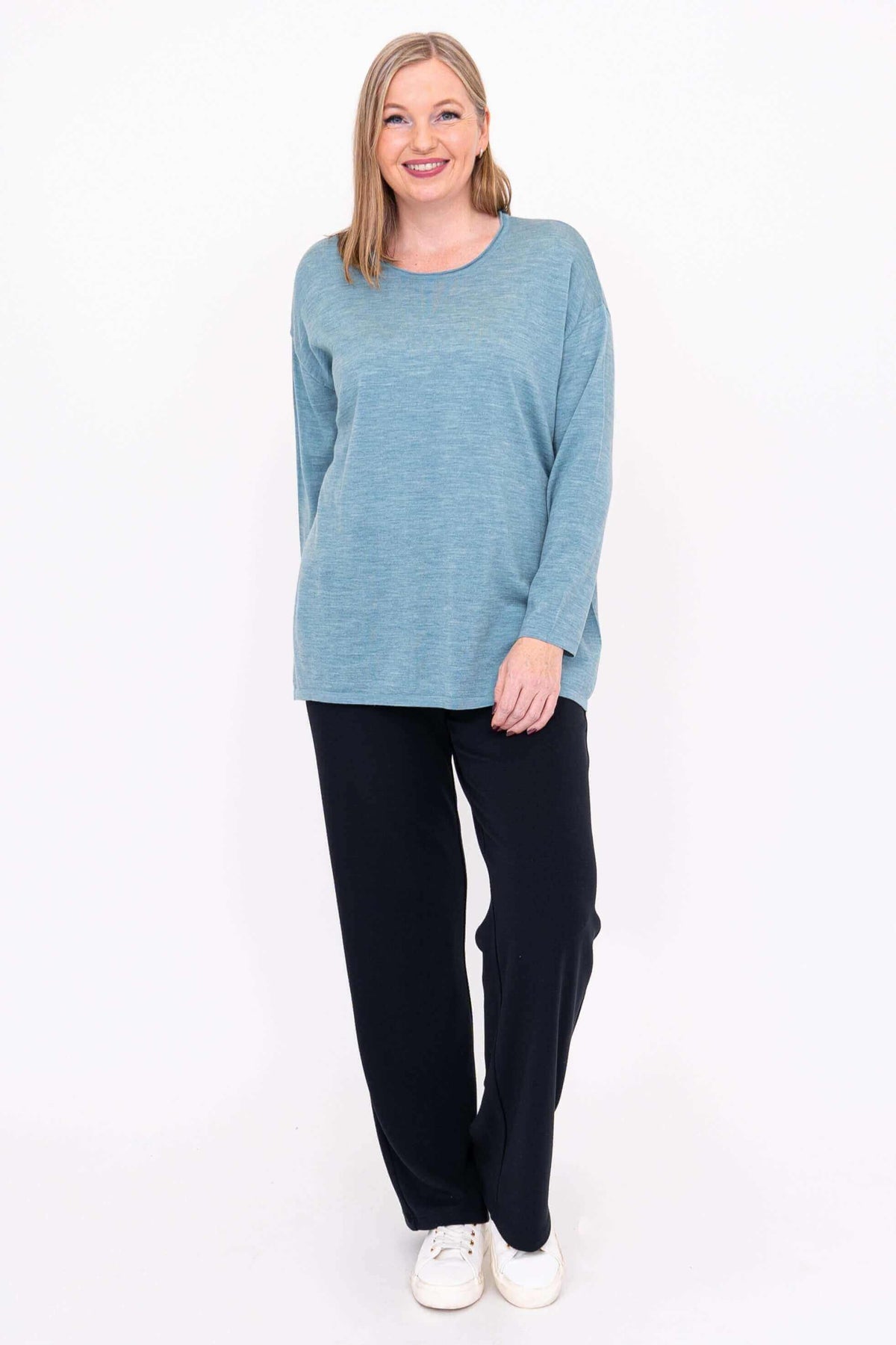 Smiling woman in blue Merino wool sweater and black pants, standing