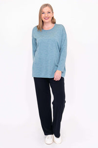 Smiling woman in blue Merino wool sweater and black pants, standing