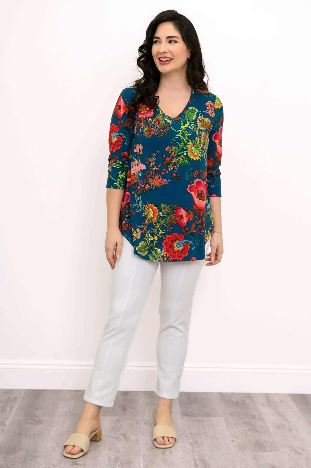 Woman smiling in a blue V-neck floral top with white pants, standing casually